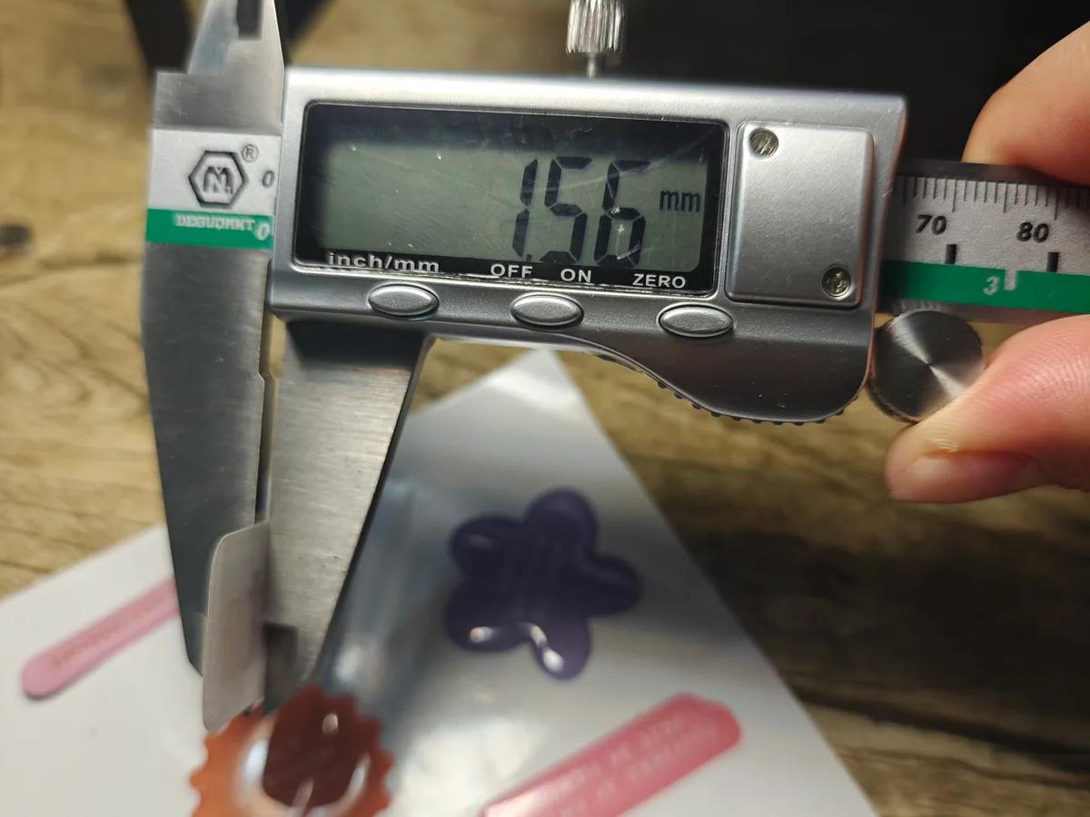 Digital caliper measurement shown above a sheet of resin domed label samples