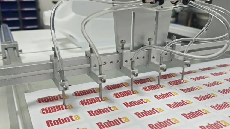 Multiple dispensing nozzles applying resin to repeat Robota label sheets