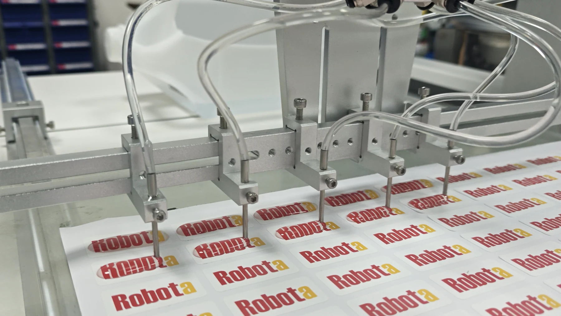 Multiple dispensing nozzles applying resin to repeat Robota label sheets
