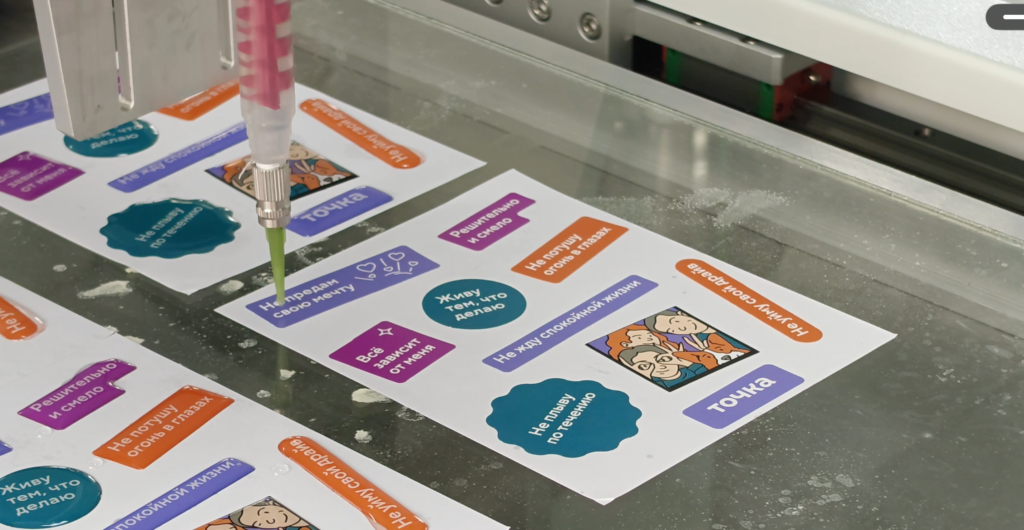 DJ771 single-needle epoxy dispensing onto mixed-layout stickers on a printed coated-paper sheet